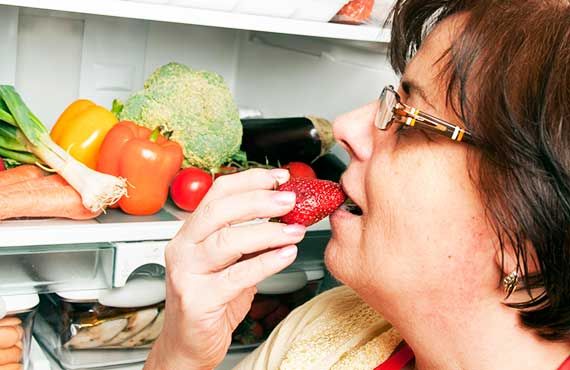 Kvinde spiser jordbær fra køleskabet